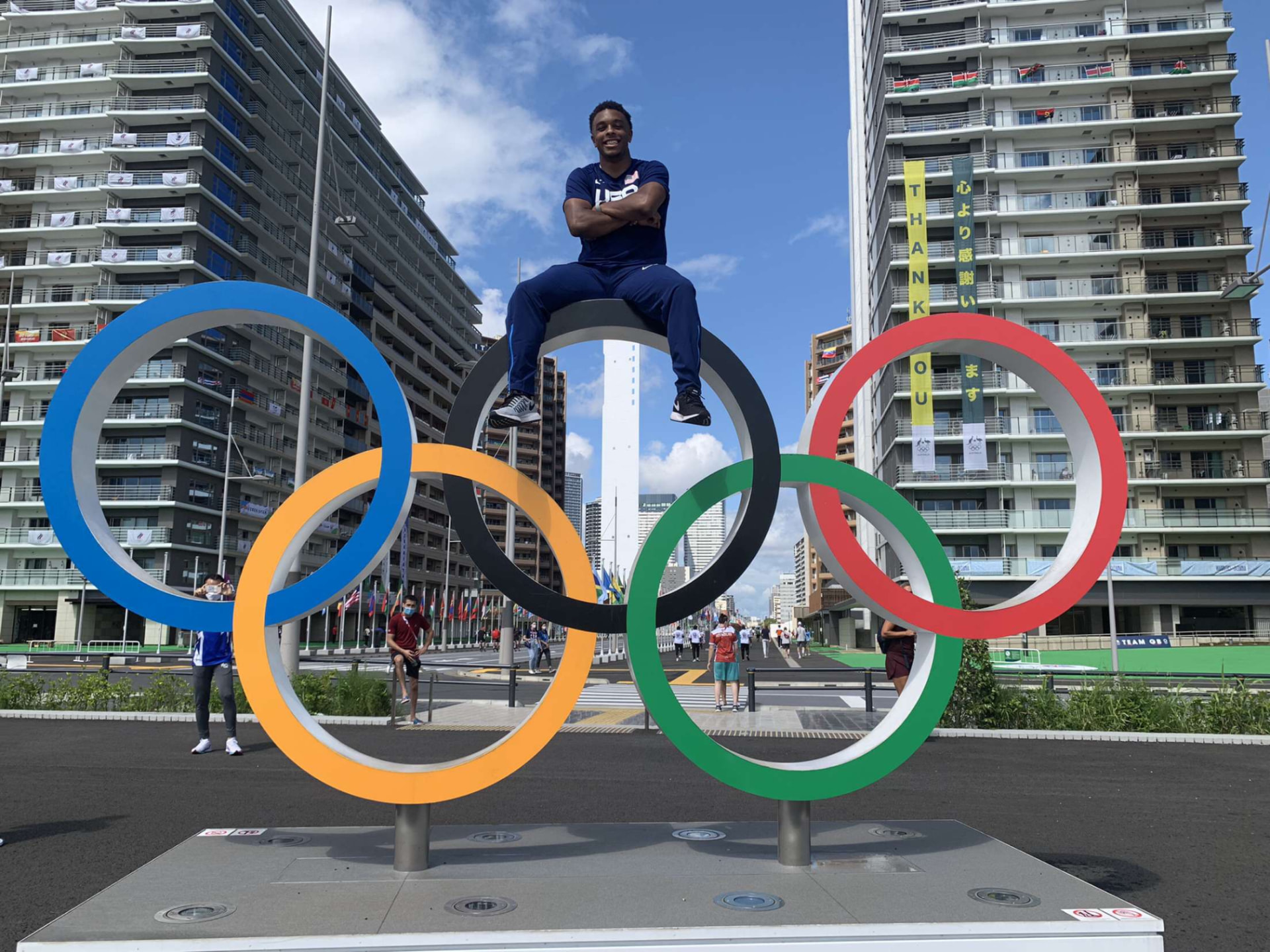 Micah Williams in Team USA gear sitting atop the Olympic rings at the Tokyo Olympic Village